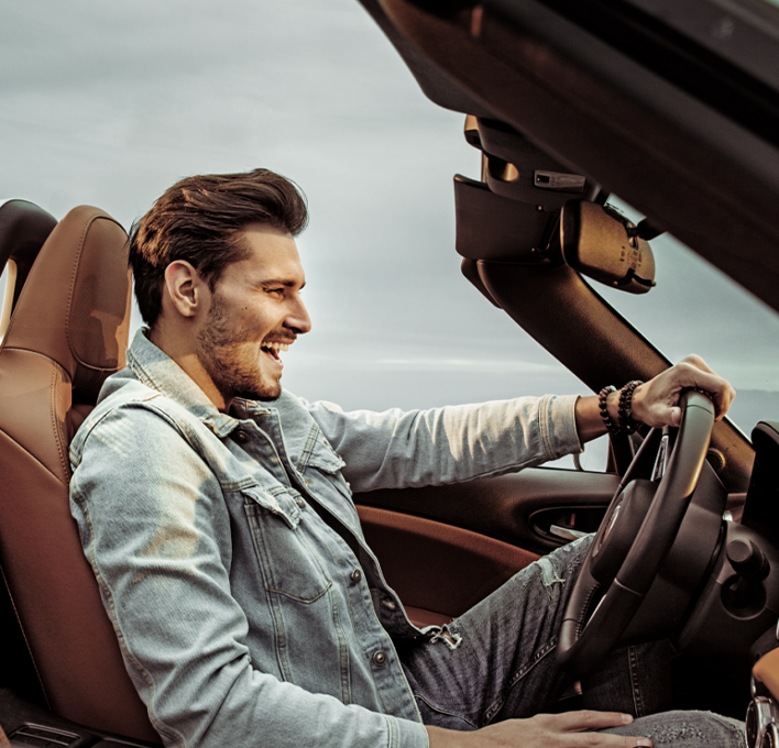 Man wearing jean jacket and smiling while driving a convertible car