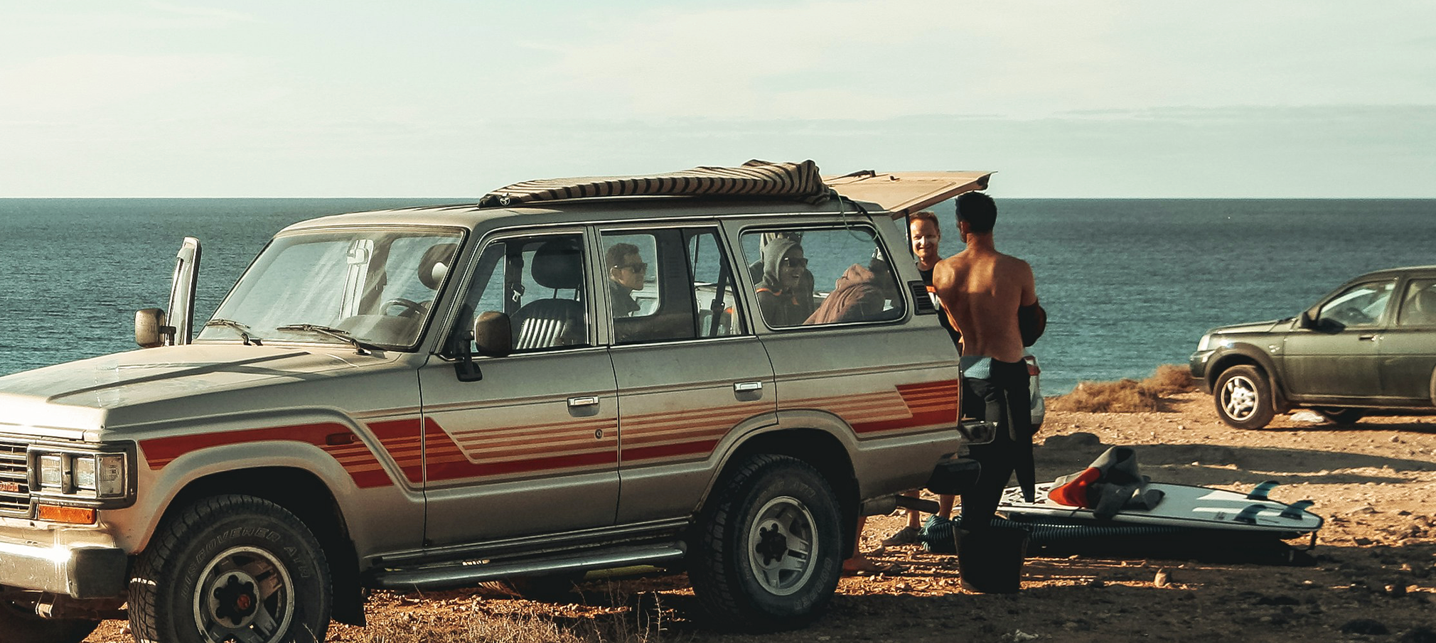 Group of friends hanging out in the back of a SUV with a view of the ocean behind them