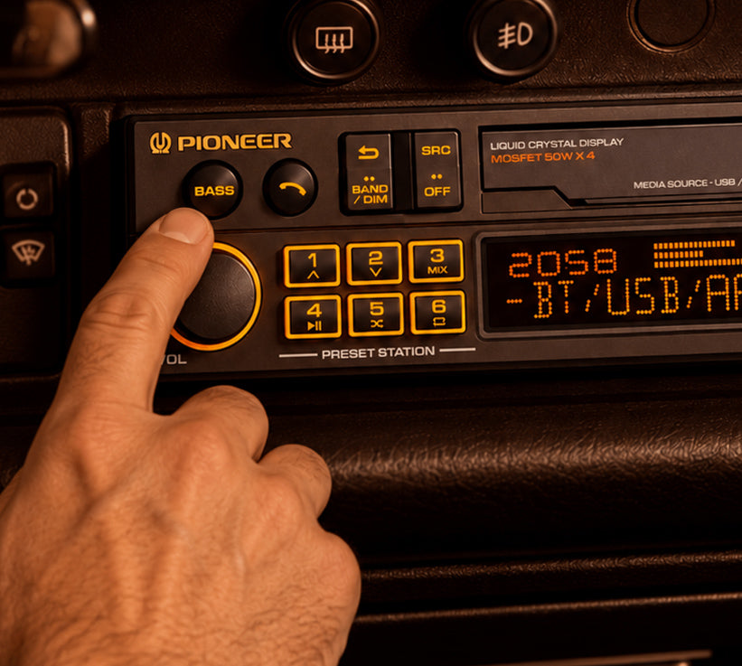 A close-up of a hand pressing the bass button on a Pioneer car stereo headunit dashboard, with the display showing BT/USB connection options.