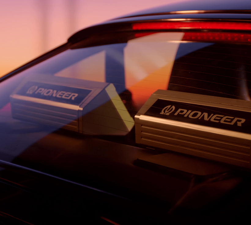 Two Pioneer car window tint trim pieces mounted on the rear window of a black vehicle, shown in warm sunset light with reflections.